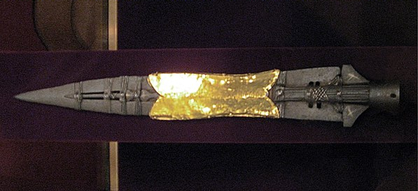 Fotografía de la punta de la Lanza del Destino, envuelta en una funda dorada y con un clavo sujeto con hebras metálicas en su centro.