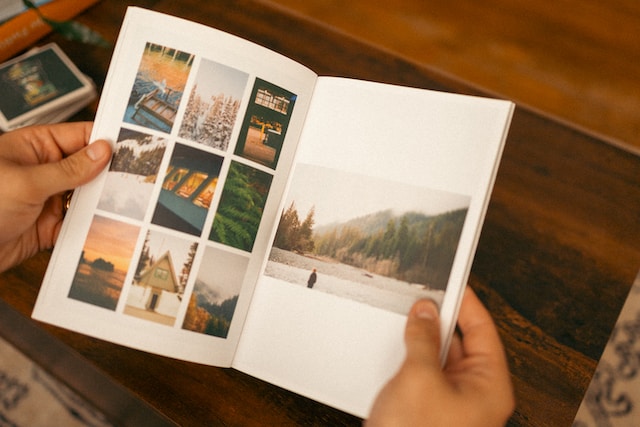 Una persona con un libro abierto en el que se ve una colección de pequeñas fotografías de paisajes naturales montañosos.