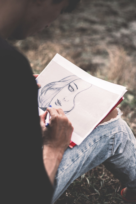 Un cuaderno en el que un hombre que queda fuera de plano está dibujando el rostro de una mujer.